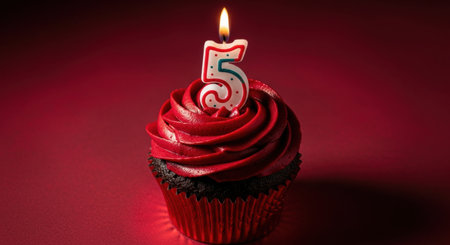 A delicious chocolate cupcake with rich red frosting and a lit number 5 birthday candle, set against a vibrant red background. Perfect for celebrations.の素材