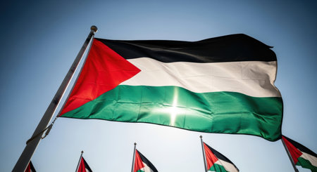 The palestinian flag waves proudly against a bright blue sky, illuminated by sunlight. This national symbol represents identity, sovereignty, and the palestinian people.の素材