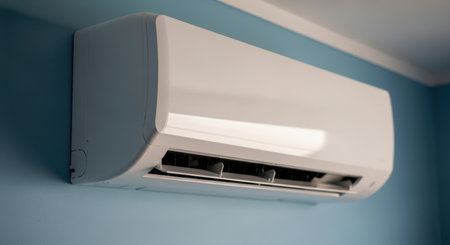 A white modern air conditioner unit is mounted on a light blue wall, providing cooling and climate control in an indoor environment.の素材