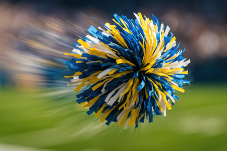 Vibrant blue, yellow, and white cheerleading pom pom captured in dynamic motion with speed blur effect. Represents team spirit, energy, and celebration on a sports field.の素材
