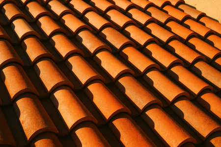 Terracotta roof tiles arranged in a classic overlapping pattern, illuminated by bright sunlight creating strong shadows. traditional mediterranean architecture detail.の素材