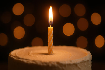 Single burning birthday candle on a frosted cake, casting a warm glow against a soft bokeh background of out of focus lights. symbolizes celebration, wishes, and special moments.の素材