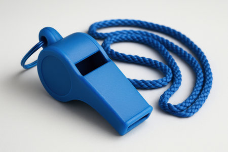 Bright blue plastic whistle with a matching twisted cord lanyard, resting on a light surface. symbolizes authority, sports, coaching, and safety.の素材