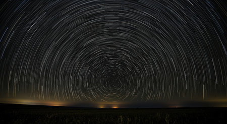 Star trails creating concentric circular patterns in the dark night sky, captured with long exposure photography above a subtle horizon, illustrating earth rotation.の素材