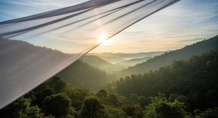 Golden sunrise over a lush mountain valley, with mist filling the low lying areas, viewed through a gently waving translucent white fabric.の素材
