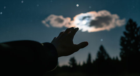 Human hand reaching up towards the bright moon and twinkling stars in a dark night sky. concept of hope, dream, and aspiration for the future.の素材