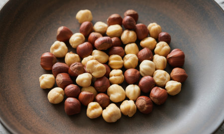 Whole roasted hazelnuts, both peeled and unpeeled, scattered on a matte dark brown ceramic plate. a healthy and nutritious snack, rich in flavor and texture, perfect for cooking or baking.の素材