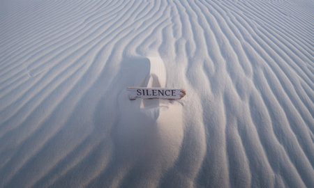 Word silence written on a small wooden plank partially buried in pristine white sand dunes with natural ripples. represents peace, quiet, and solitude in a vast desert landscape.の素材
