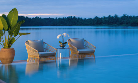 Luxurious infinity pool with stylish rattan lounge chairs and a glass table adorned with orchids, offering a serene view of a calm deep blue lake at dawn. tropical plant in a pot adds to the tranquil resort ambiance.の素材