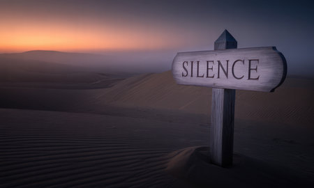 Wooden signpost with SILENCE text prominently displayed in a vast, serene desert landscape. undulating sand dunes stretch under a colorful dawn sky, evoking concepts of peace, solitude, and quiet reflection.の素材