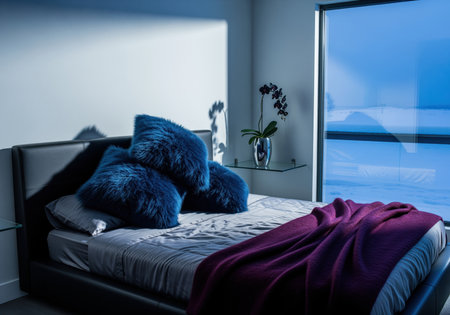 Contemporary bedroom featuring a bed with plush blue pillows and a purple throw blanket. dramatic blue lighting casts shadows, creating a moody atmosphere by a large window overlooking a serene winter landscape.の素材