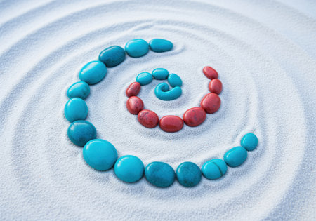 Smooth turquoise and coral red river stones meticulously arranged in a perfect spiral pattern on a surface of fine white sand, creating a serene and balanced visual composition. represents harmony, balance, and meditation.の素材