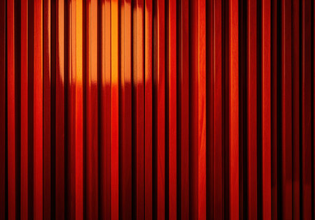 Vertical strips of exotic deep red padauk wood arranged in a uniform linear pattern. high contrast with bright light reflection and dark shadows creates a rich textured background.の素材