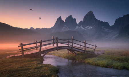 Wooden bridge spans a tranquil river in a misty mountain valley at dawn. jagged peaks rise above the fog, creating a serene and peaceful natural landscape.の素材