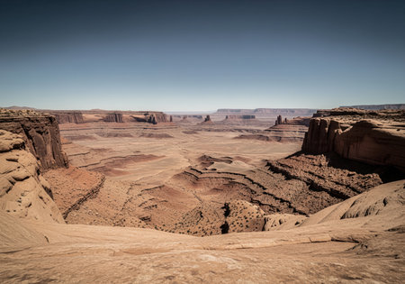 Vast arid desert landscape with deep canyons, towering mesas, and rugged rock formations under a clear blue sky. expansive geological formations showcase the dry, natural environment.の素材
