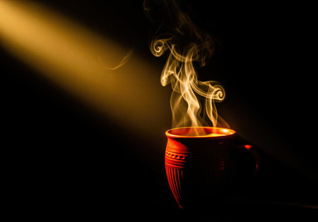 Steaming hot tea in a traditional red clay kulhad, dramatically illuminated by a golden light beam against a dark background, evoking warmth and comfort.の素材