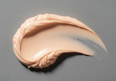 Thick pale peach facial moisturizer artfully smeared in a swirling pattern on a cool, matte grey surface. represents skincare, beauty, and cosmetic product texture.の素材