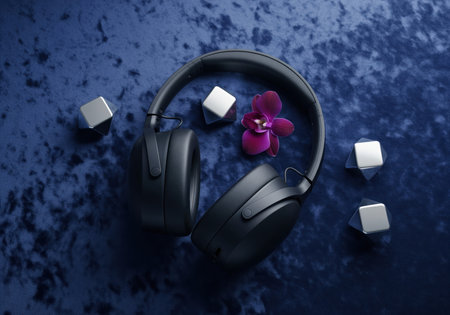 Matte black noise canceling headphones, a vibrant purple orchid, and reflective silver cubes arranged on a luxurious deep indigo blue velvet surface. modern audio technology meets elegant aesthetics.の素材
