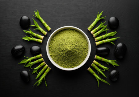 Vibrant matcha green tea powder in a central bowl, artfully arranged with fresh bamboo stalks and polished black stones on a dark background. evokes themes of spa, zen, and natural health.の素材