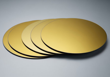 Five perfectly polished gallium arsenide wafers stacked on a light surface, showcasing their uniform deep gold color and smooth, reflective finish. ideal for technology and material science concepts.の素材