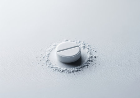 Round white pill with a dividing score, resting on a small pile of crushed powder on a clean, light surface. represents medicine, dosage, and health.の素材