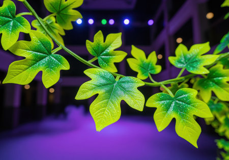 Vibrant artificial green and yellow leaf decoration with sparkling texture, arranged on a decorative vine. blurry purple and dark background with bokeh lights creates a festive atmosphere.の素材