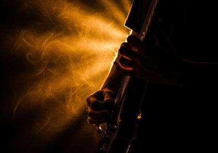 Musician hands playing electric guitar in a dramatic silhouette against a dark background, highlighted by intense amber backlighting and smoke during a live concert performance.の素材