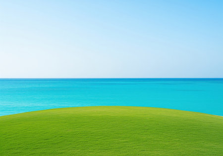 Lush green grass field foreground meeting the horizon line of vibrant turquoise ocean water and a bright blue sky. perfect nature background for design and copy space.の素材