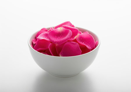 Fresh pink rose petals covered in small dew drops, neatly arranged inside a smooth white ceramic bowl. high key studio shot emphasizing freshness, romance, beauty, and spa concepts.の素材