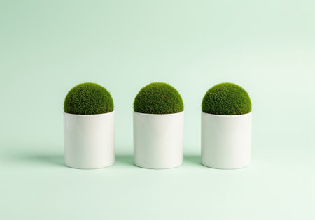 Three perfectly aligned green moss balls planted in white cylindrical ceramic planters against a pale green background, emphasizing minimalism, symmetry, and indoor gardening.の素材