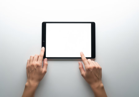 Hands of a woman interacting with a black digital tablet device displaying a blank white screen mockup. clean, top view shot for technology, business, and app design concepts.の素材