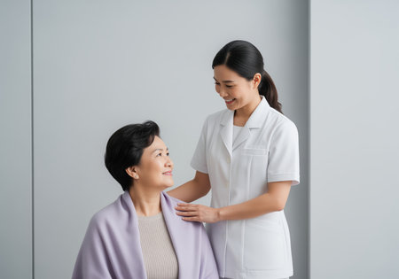 Asian healthcare worker supporting a senior woman patient with a reassuring smile and gentle touch in a clean medical environment, symbolizing trust and care.の素材