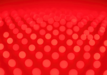 Uniform field of luminous, out of focus red bokeh circles arranged in a repeating pattern. abstract, vibrant, and energetic background texture suitable for festive, technological, or romantic themes.の素材