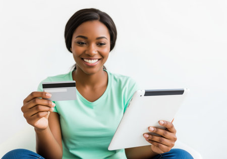 Smiling young african woman holding a credit card and digital tablet, engaging in secure online transaction, e commerce, or mobile banking.の素材