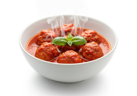 Savory italian meatballs simmering in rich tomato marinara sauce, topped with fresh basil and emitting steam, presented in a white serving bowl.の素材