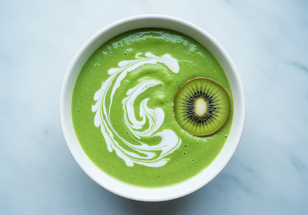 A vibrant green smoothie or soup served in a white bowl, beautifully garnished with a slice of kiwi and a decorative swirl of white cream. perfect for healthy eating concepts.の素材
