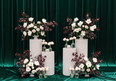 Symmetrical display of white flowers and dark red leaves in urns atop white textured pedestals, creating a dramatic and luxurious atmosphere for a wedding or gala event.の素材