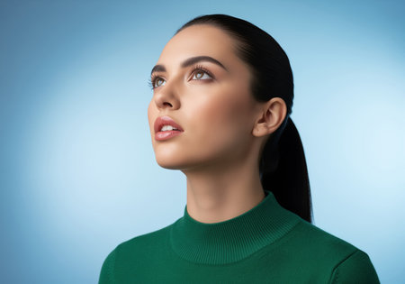 Studio portrait of a beautiful young woman with dark hair pulled back, wearing a green turtleneck. she looks upwards with a contemplative and focused expression, suggesting aspiration or deep thought.の素材