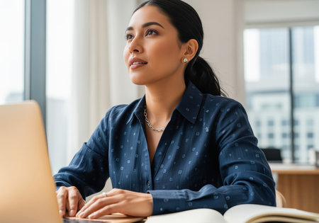 A thoughtful young professional woman sits at her desk, looking away from her laptop, contemplating business strategies and future growth.の素材