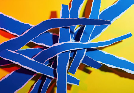 Torn strips of deep blue paper are dynamically arranged and overlapped, creating an abstract texture against a vibrant yellow and orange background. strong color contrast and shadows enhance the graphic design element.の素材
