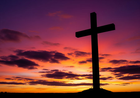 Large christian cross silhouette standing on a hill against a vibrant, dramatic sunset sky featuring purple, orange, and red clouds. symbolizing faith, hope, and spirituality.の素材