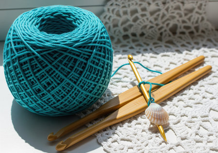 A large ball of vibrant teal cotton yarn sits next to two wooden crochet hooks adorned with a small seashell charm, resting on delicate white lace. this setup suggests a relaxing hobby or craft project.の素材