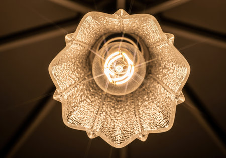 Close up shot of a bright, warm light bulb illuminating a decorative, textured glass fixture from below. this detail emphasizes vintage style and interior lighting design.の素材
