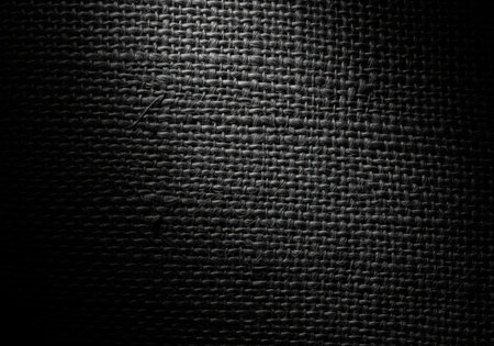 Dark charcoal grey burlap textile texture featuring a tight woven pattern and rough natural fiber detail, highlighted by dramatic spotlighting.の素材