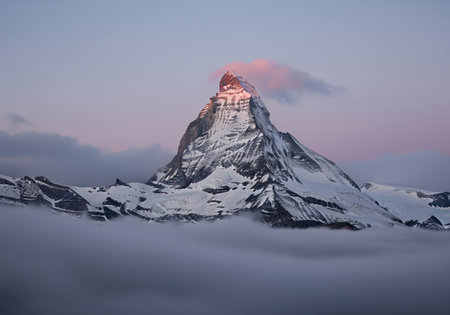 Matterhorn mountain peak covered in snow and ice, dramatically illuminated by pink alpenglow, standing tall above a thick layer of atmospheric fog and clouds in the swiss alps.の素材