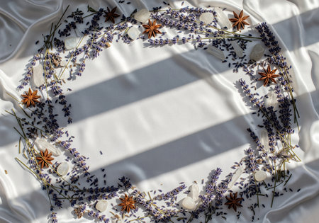Lavender sprigs, star anise, and quartz crystals arranged in a wreath shape on shimmering white silk fabric. dramatic window shadows cross the empty center space.の素材