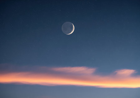 Crescent moon and distant stars suspended in the deep blue twilight sky. a thin layer of clouds near the horizon is illuminated with warm orange light.の素材