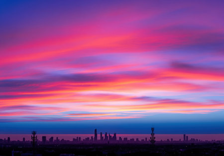 Dramatic twilight sky painted in vibrant pink, fuchsia, and purple hues above a dark silhouette of a modern urban city skyline. atmospheric and colorful.の素材