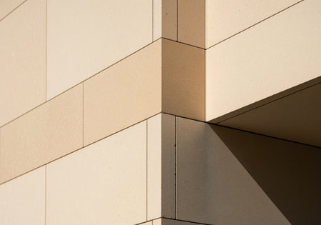 Modern architectural detail featuring the precise corner joint of a building facade constructed with large, smooth beige stone blocks. strong geometric lines and contrast between sunlit surfaces and deep shadow.の素材