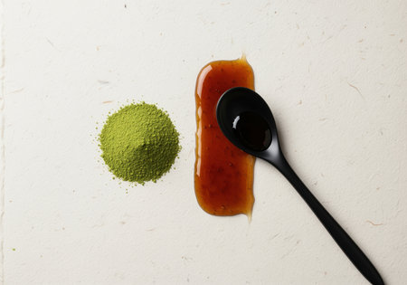 Vibrant green matcha tea powder pile next to a thick smear of glossy caramel sauce, featuring a black spoon on a textured white surface. minimalist flat lay studio shot.の素材